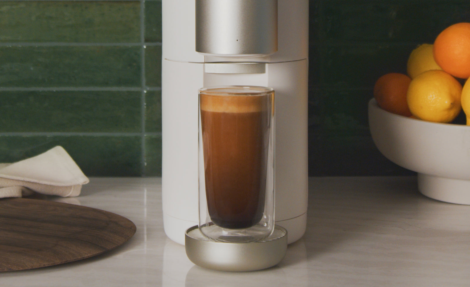 A tall glass cup having just been filled up, still sitting inside of a white cumulus coffee machine.