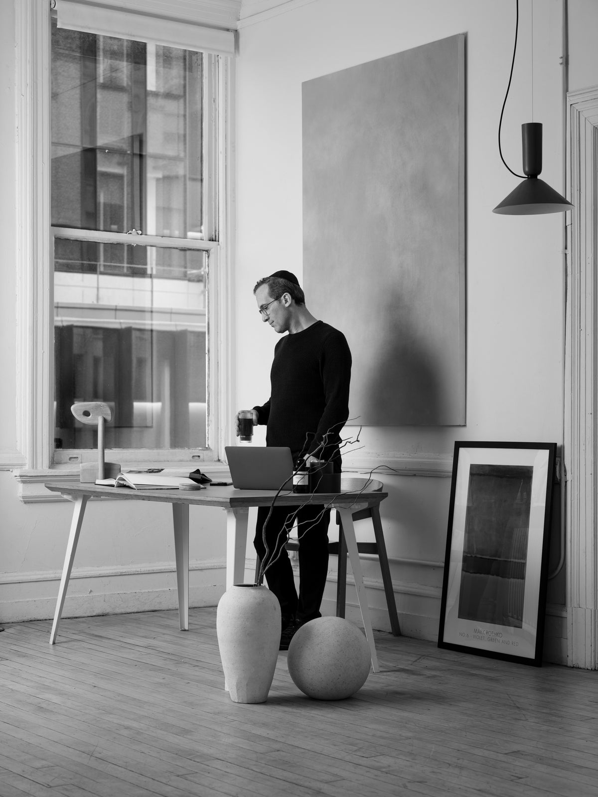 Wide shot of Cumulus Founder Mesh Gelman standing in front of a desk in a modern office holding a cup of coffee