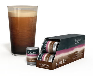 An opened pack of Sospeso medium roast coffee capsule next to a cup of coffee