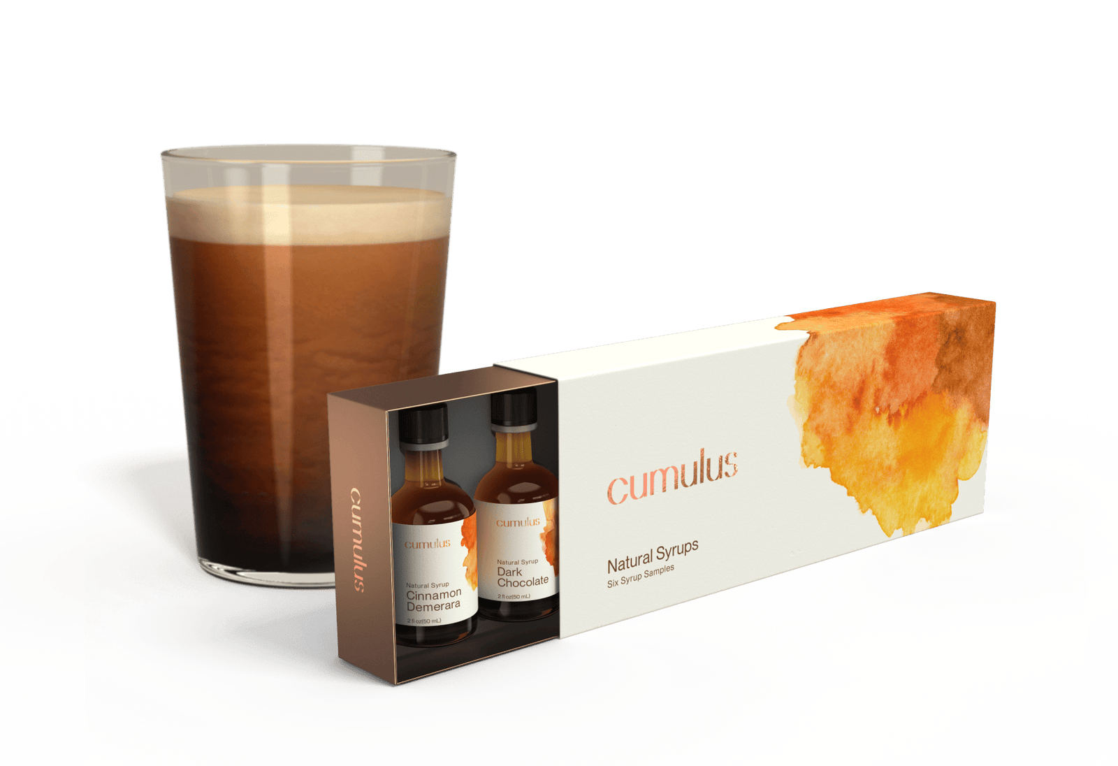 A partially opened box of Cumulus Syrups sitting in front of a large cup of cold brew coffee. The box is labeled "Natural Syrups - six syrup samples" and the two visible flavors are "Cinnamon Demerera" and "Dark Chocolate"