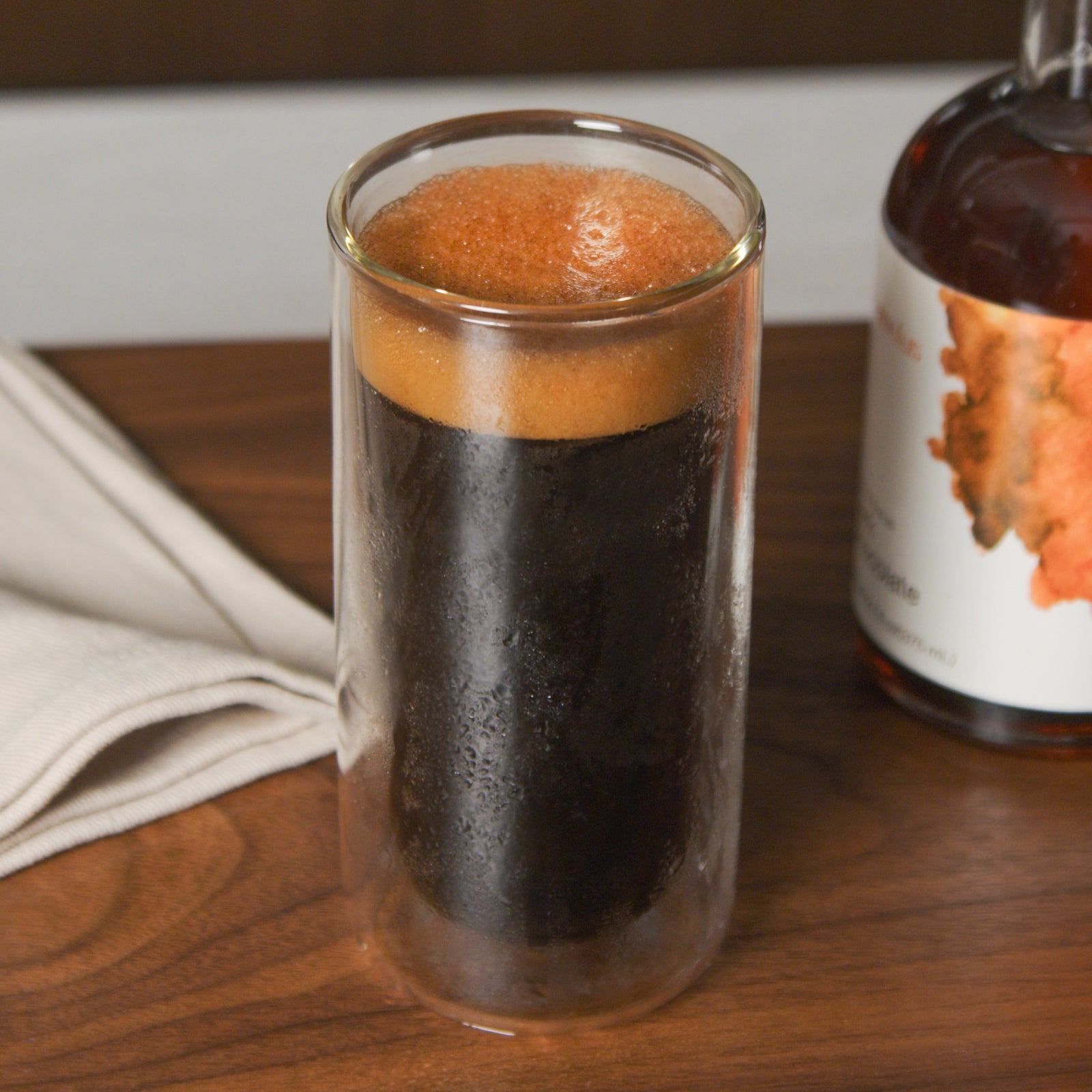 A close up showing a tall glass cup full of cold brew. The outside of the glass has condensation on it and there is a bit of foam on top of the coffee.