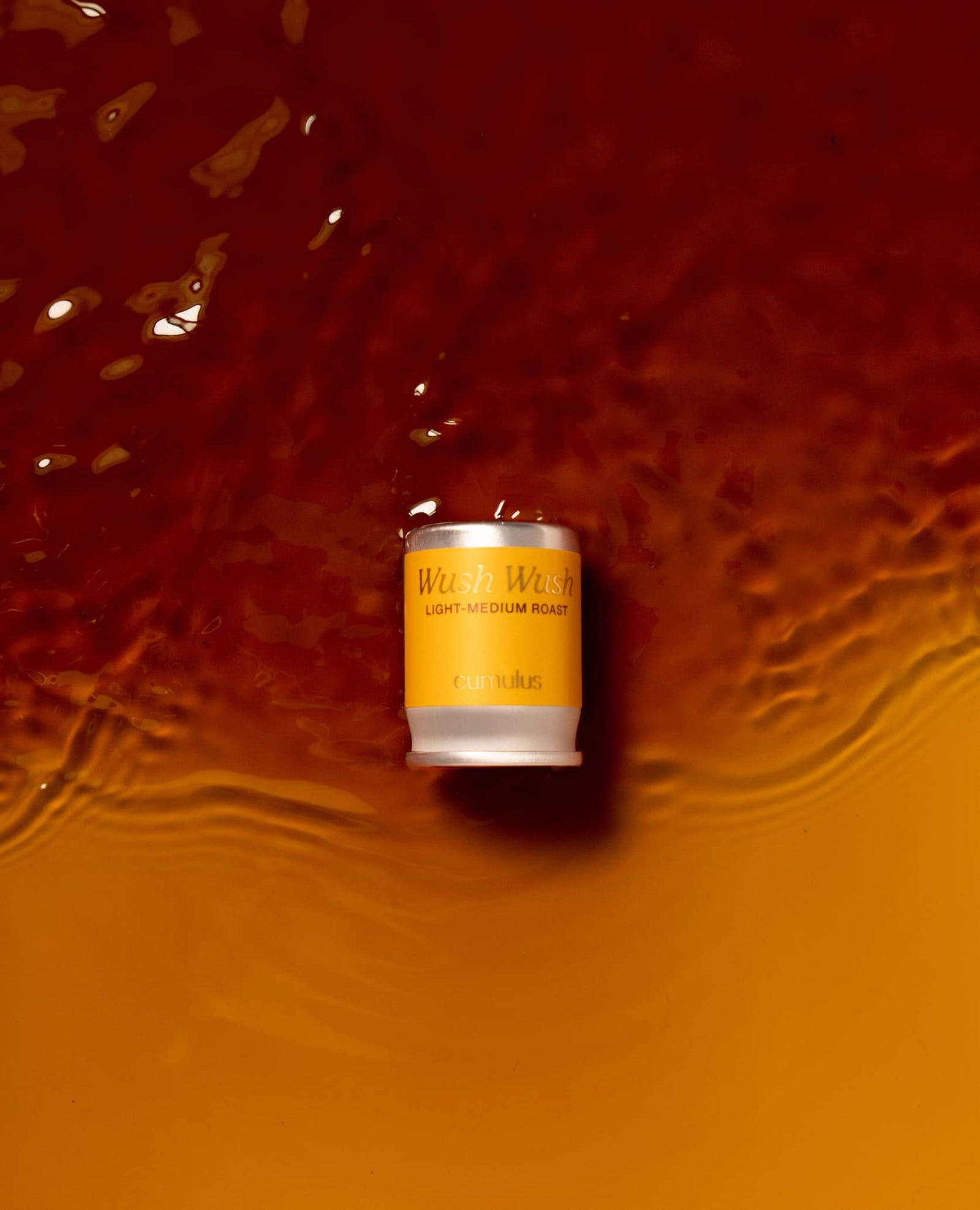 A flavor capsule laying partially submerged in coffee as if on a beach. The flavor is "Wush Wush - light medium roast"