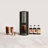 Sleek black coffee maker with a glass of brewed coffee beneath, surrounded by flavor pods and three cold brew concentrate bottles