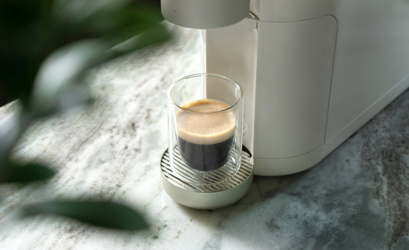 A short glass cup having just been filled up, still sitting inside of a white cumulus coffee machine.