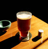 A cup sitting on a table next to an empty bowl and a flavor capsule. The cup is full of cold brew with a thin layer of foam on top.