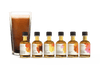 A set of six cumulus flavor syrup bottles sitting in front of a cup of cold brew coffee. The labels say "Cinnamon Demerera", "Dark Chocolate", "Yuzu Limoncello", "Madagascar Vanilla Bean", "Mole" and "Orange Piloncillo"