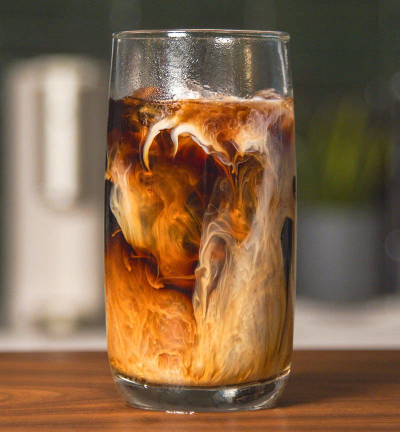 A glass full of coffee with visible swirls of milk
